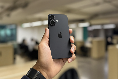 Person holding a matte black iPhone 17 in an office setting, showing rear dual-camera design