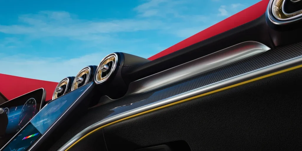 showing the luxurious interior of a Mercedes C-Class, highlighting the dashboard with sleek air vents, a prominent infotainment screen, and carbon fiber trim, all under a clear blue sky.
