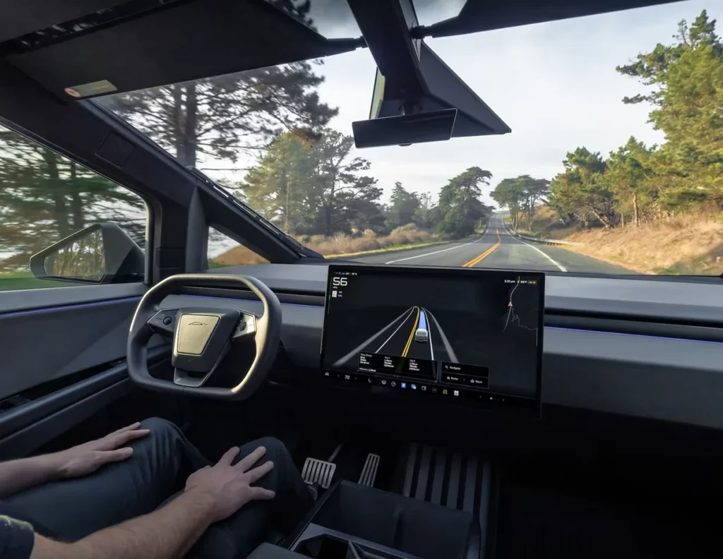 Tesla Cybertruck interior, dashboard, and yoke steering wheel, with Full Self-Driving (FSD) Beta display showing autonomous navigation on a highway.