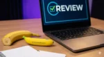 “Gemini 3 Nano Banana Pro placed next to a real banana, a notebook, and a laptop displaying ‘REVIEW’ on the screen on a wooden desk.”