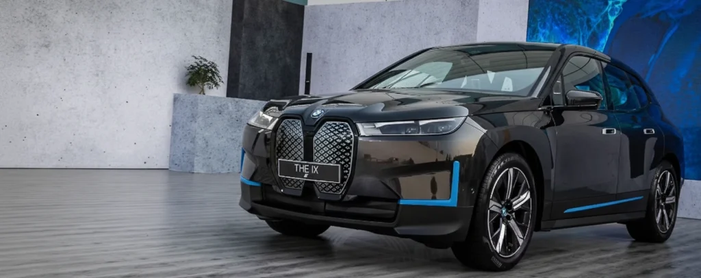 A dark-colored BMW iX electric SUV, featuring distinctive blue accents, displayed at an event with "THE iX" visible, highlighting the BMW iX Price in India (2025) as an electric SUV that redefines luxury.