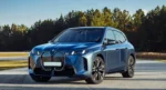 A sleek blue BMW iX electric SUV, representing the BMW iX Price in India (2025) and its role as an electric SUV that redefines luxury, on a sunlit road with trees in the background.